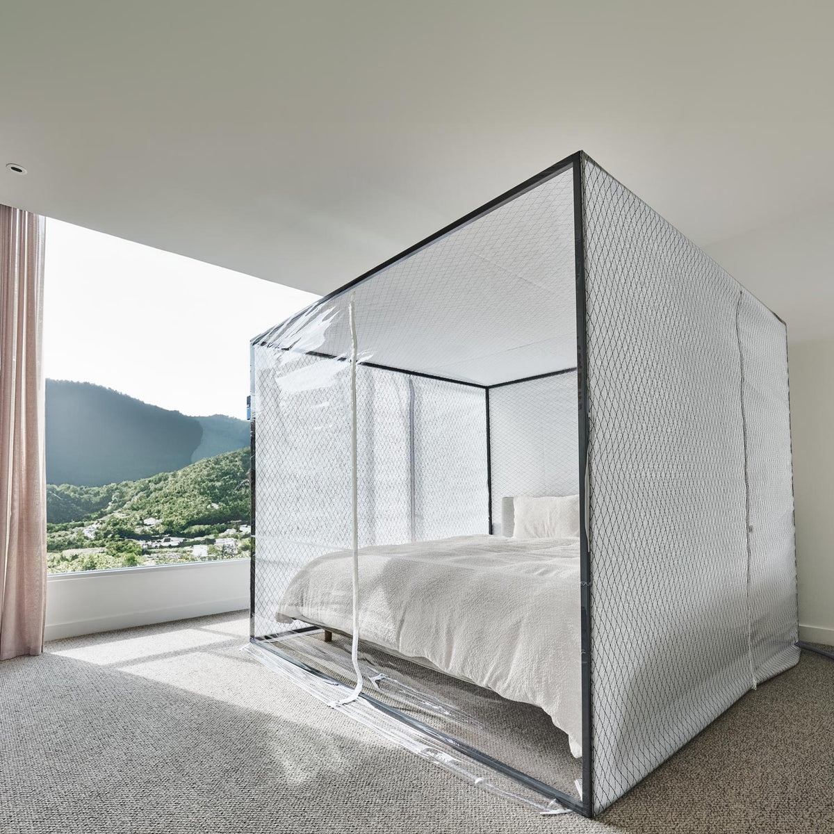 The tent seen from the corner with its clear zip door closed, green wooded hills through the window